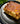 A slice of cheesy lasagna on a black plate, styled with a piece of Swiss cheese and parsley on a dark blue textured background.